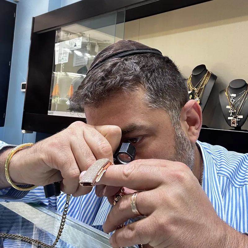 Person examining a stone-set jewelry piece through a jeweler's loupe
