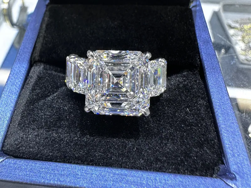 Ring with a rectangular step-cut center stone and side stones in a blue presentation box