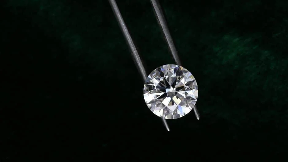 A large round polished diamond held in jeweler tweezers